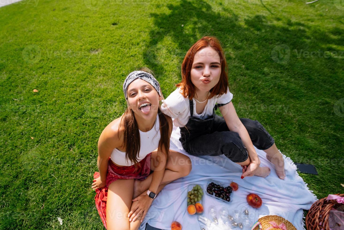 Two women having picnic together, sitting on the plaid photo