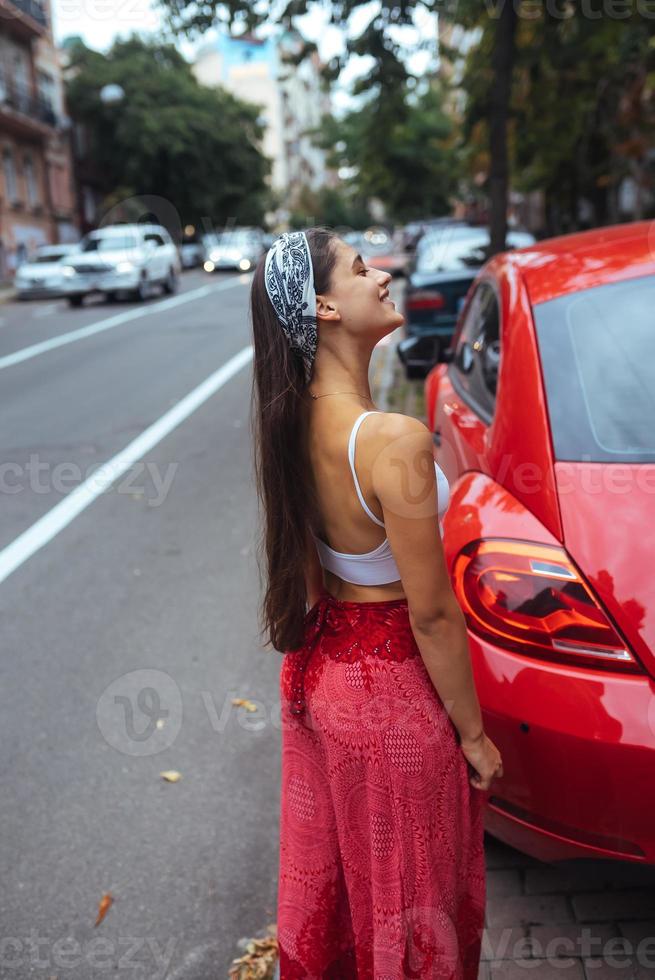 Portrait of pretty Caucasian woman standing against new red car photo