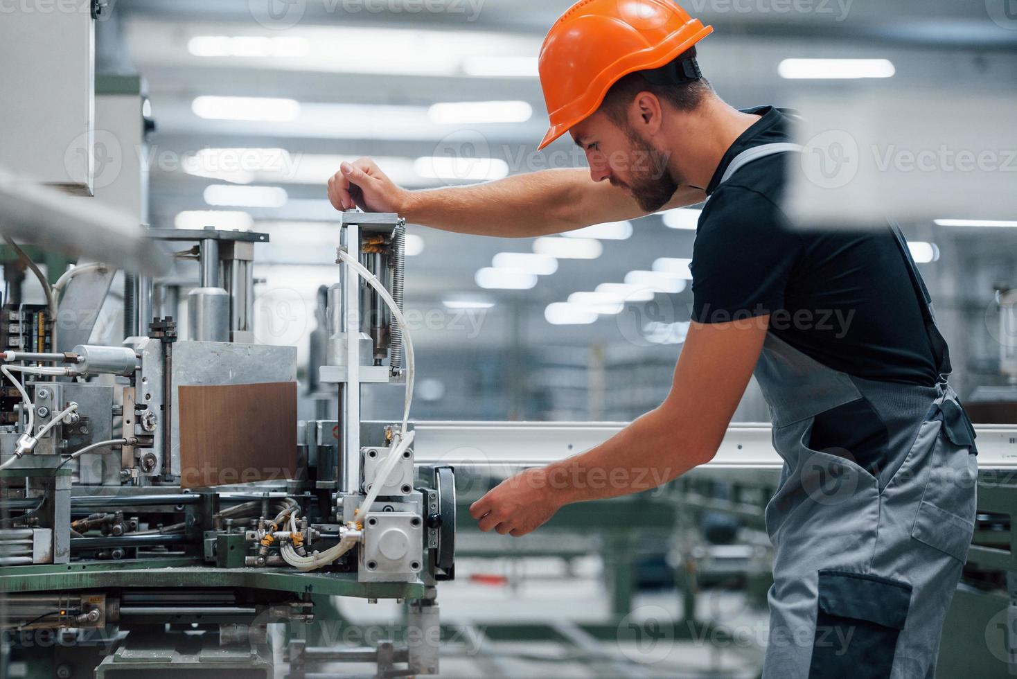 Operator of machine. Industrial worker indoors in factory. Young technician with orange hard hat photo