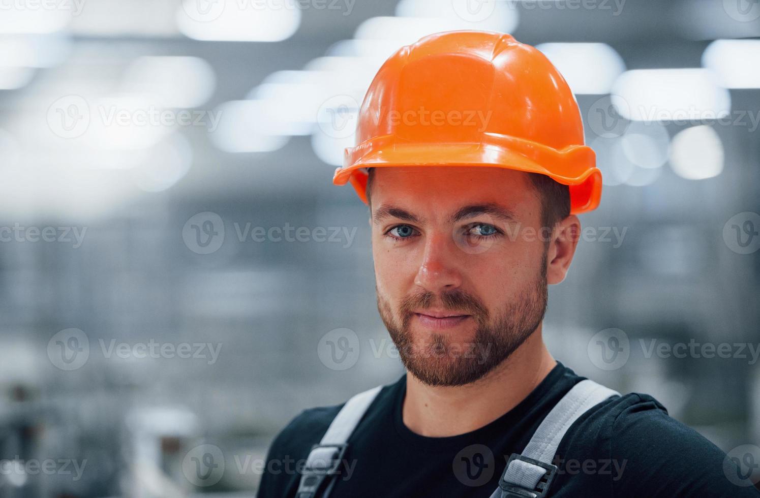 Portrait of male industrial worker indoors in factory. Young technician with orange hard hat