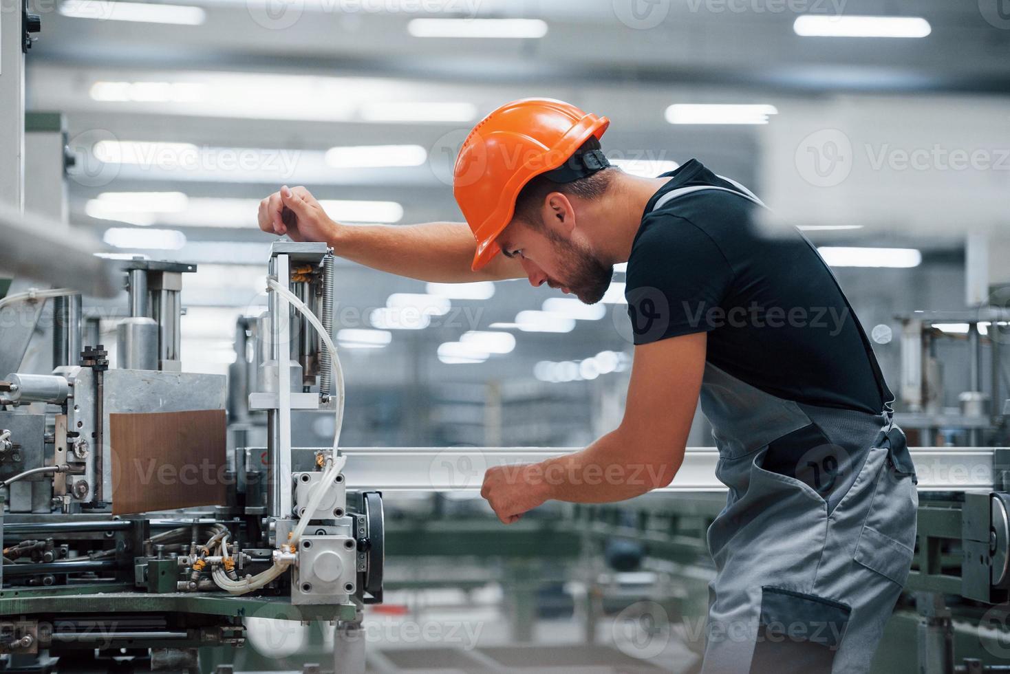 Operator of machine. Industrial worker indoors in factory. Young technician with orange hard hat photo