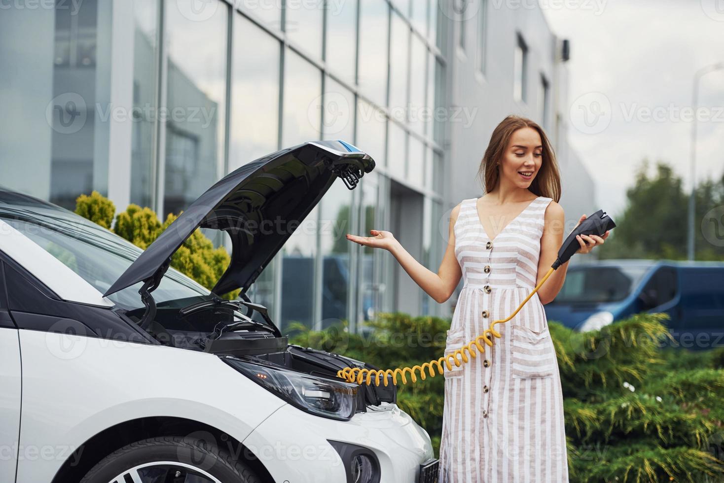 Wondering about new technology. Woman on the electric cars charge station at daytime. Brand new vehicle photo