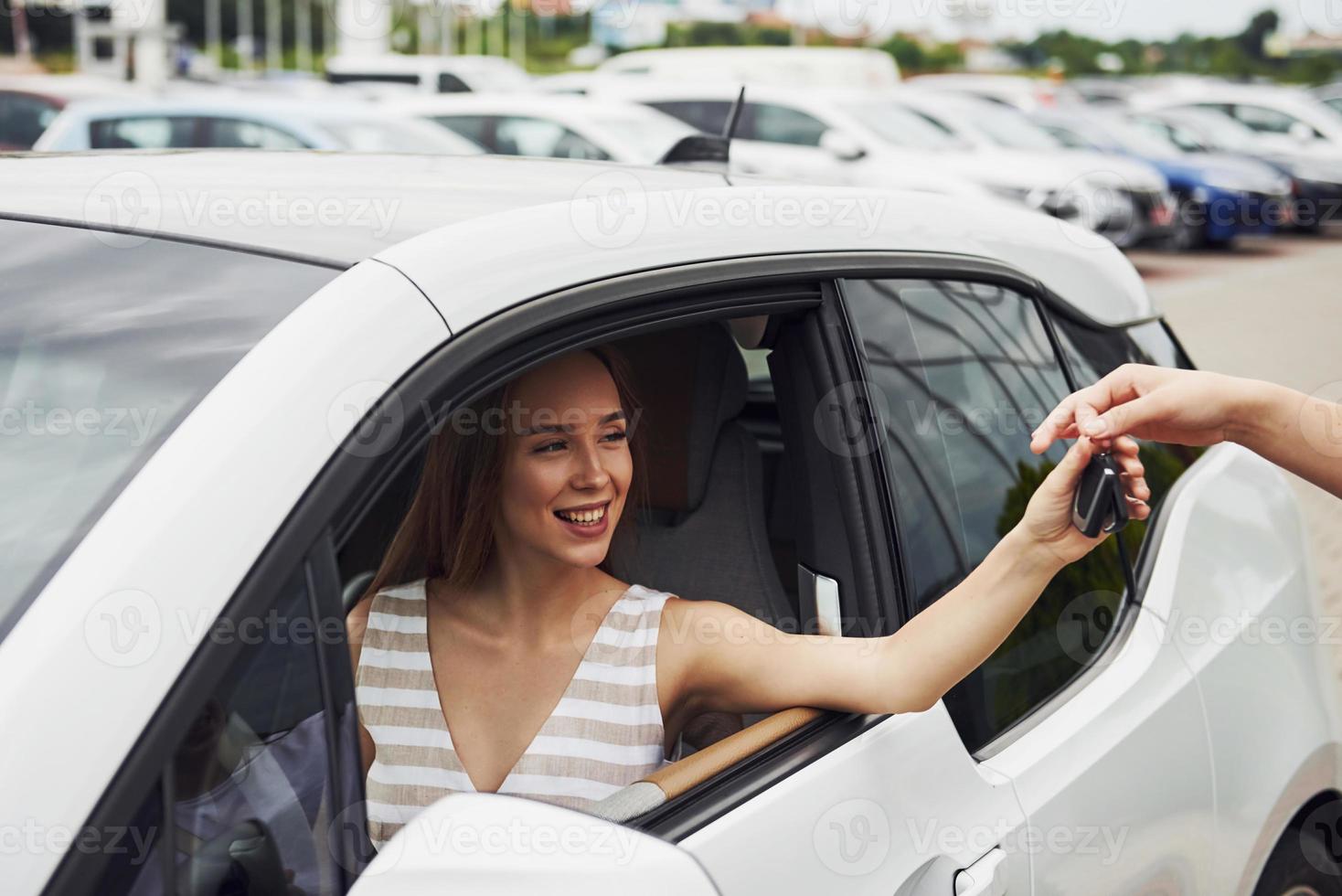 Taking keys of the car. Two people. Girl sitting in her brand new automobile photo