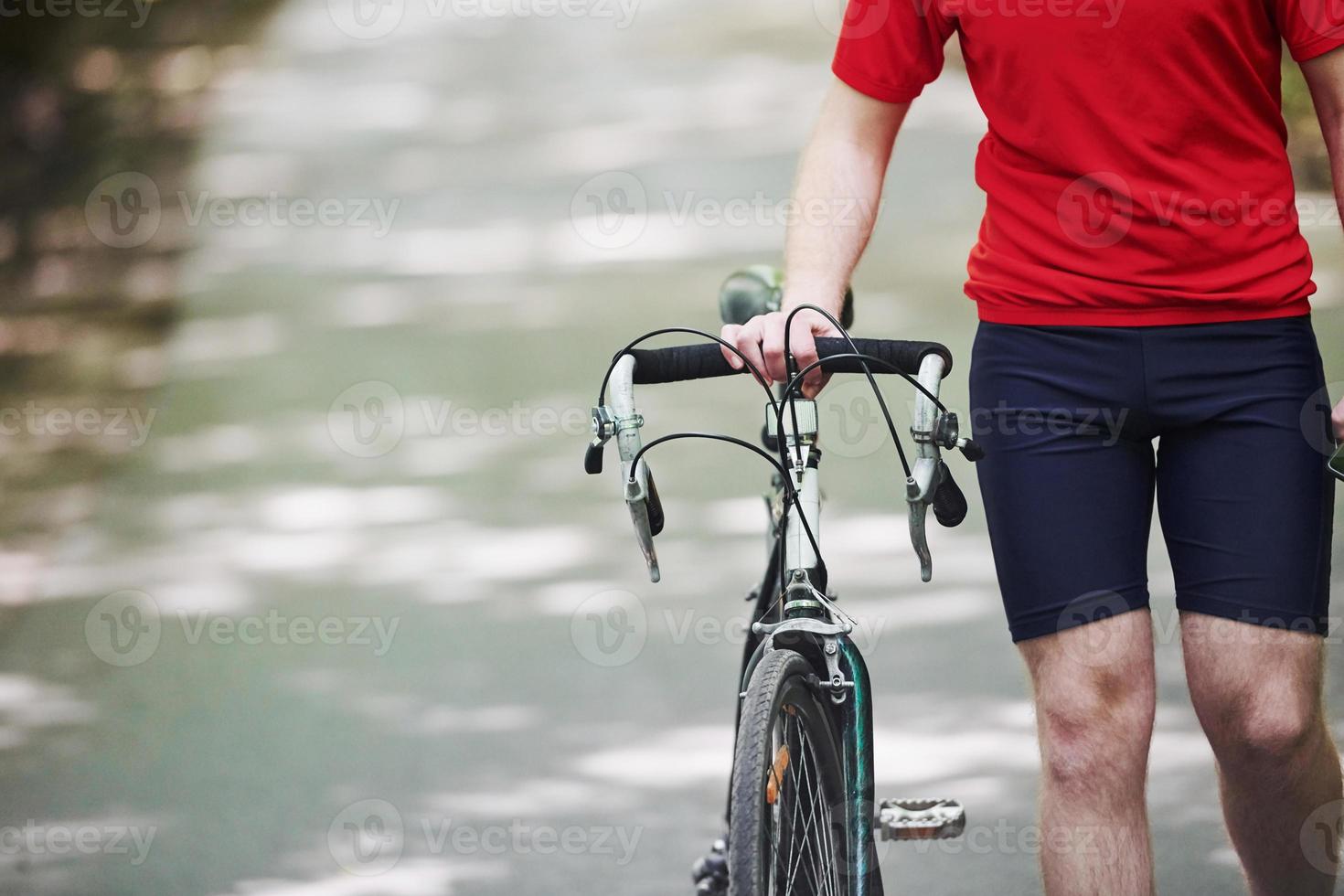 Body only. Cyclist on a bike is on the asphalt road in the forest at sunny day photo