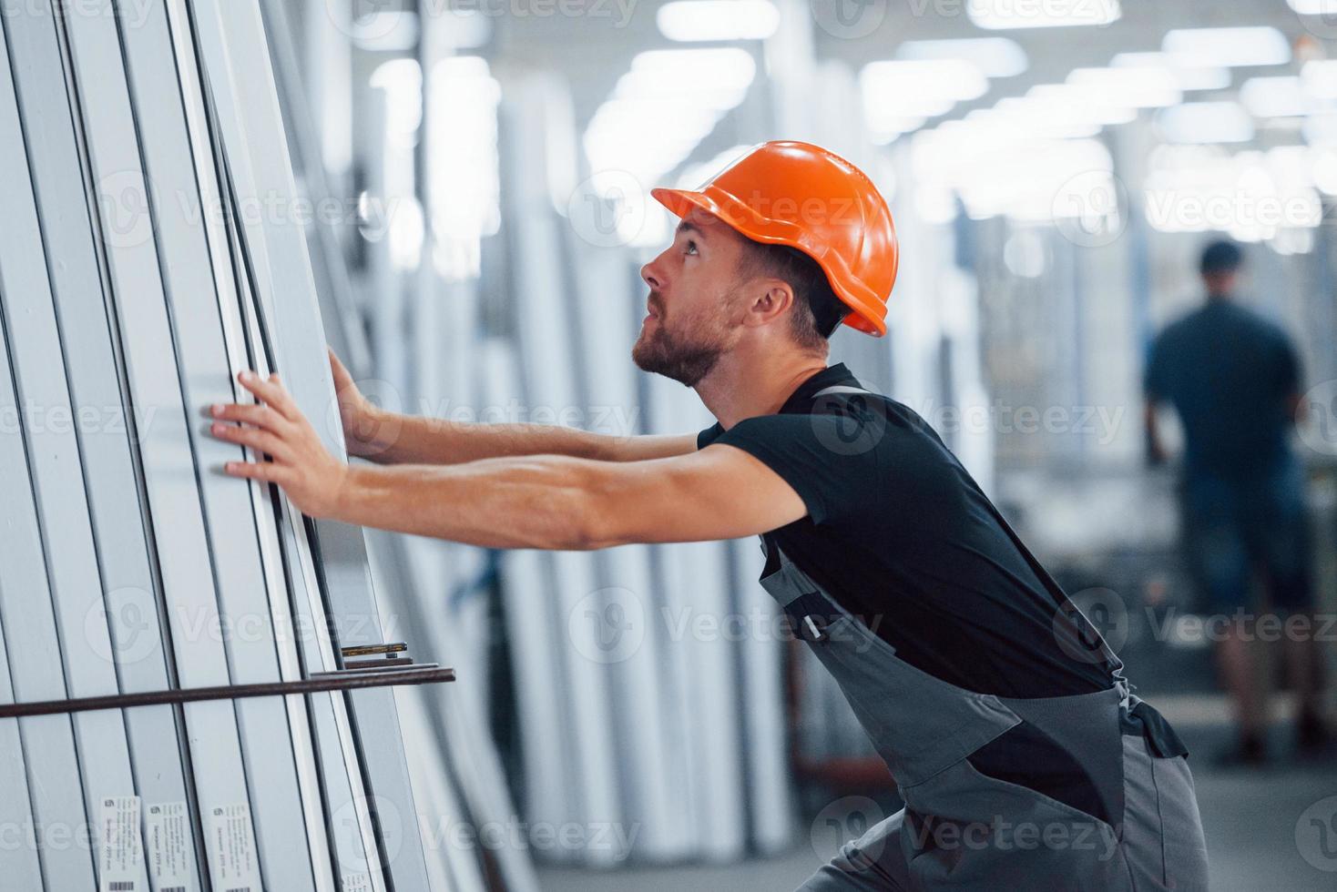 In the storage with many of objects. Industrial worker indoors in factory. Young technician with orange hard hat photo