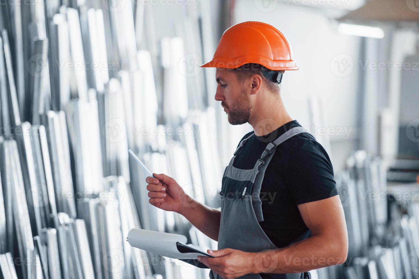 contar y controlar objetos en el almacén. trabajador industrial en el interior de la fábrica. joven técnico con casco naranja foto