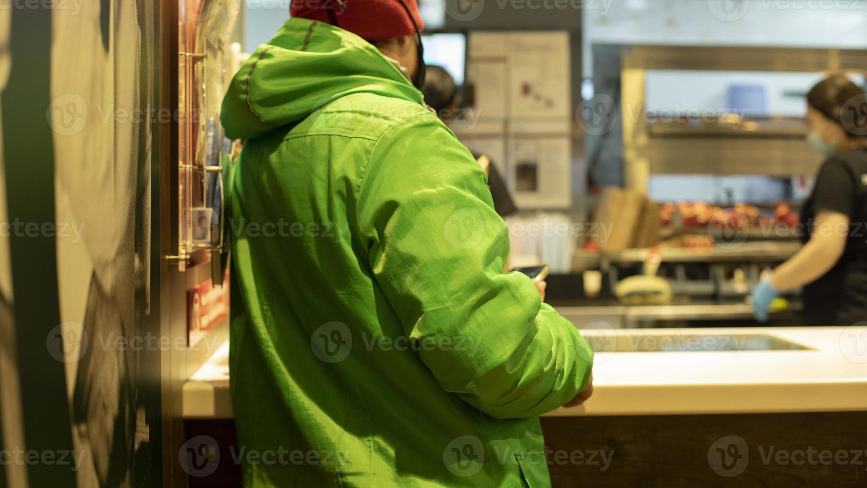 Courier picks up food at restaurant. Green jacket on courier. photo