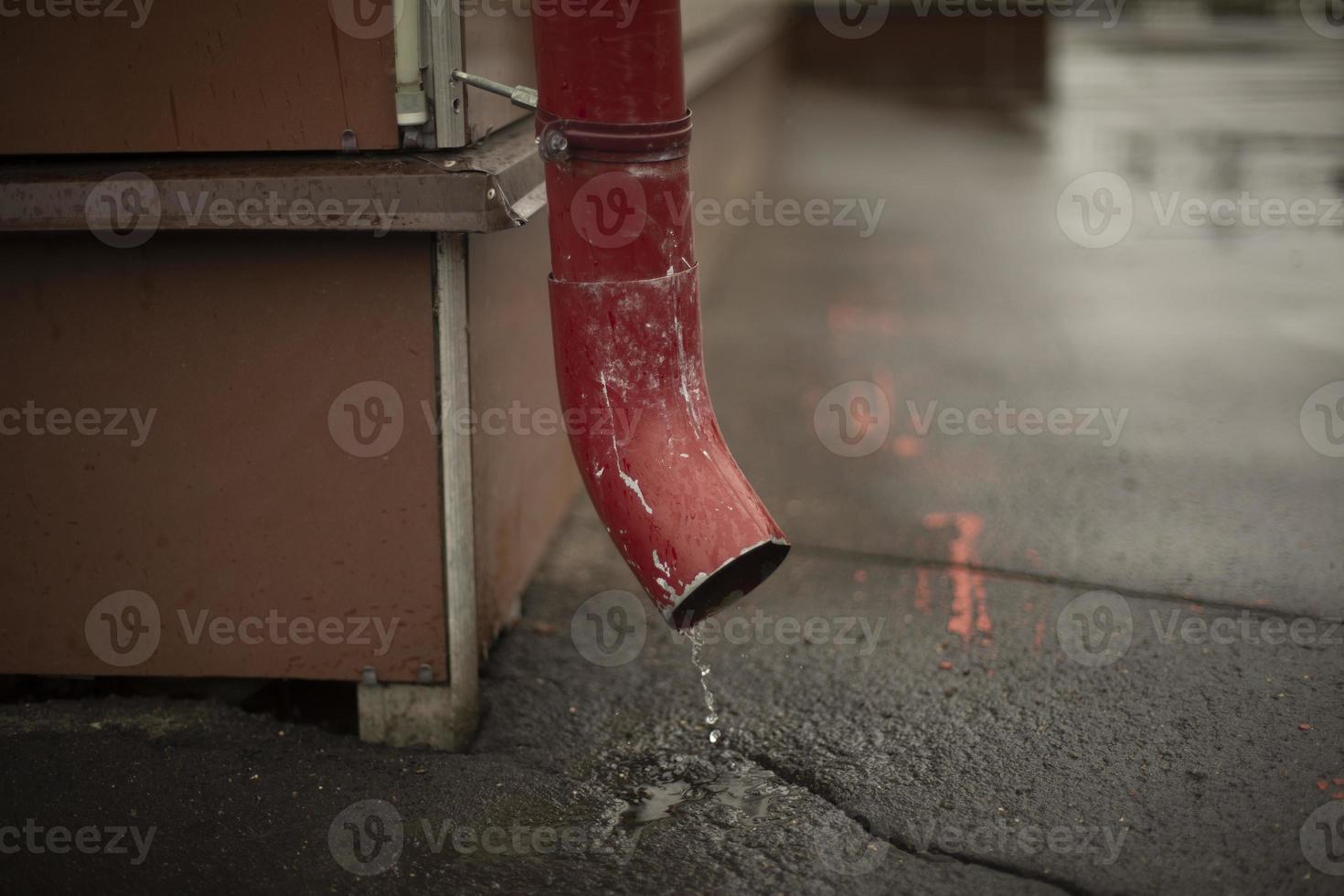 Downspout in building. Water flows from roof onto asphalt. photo