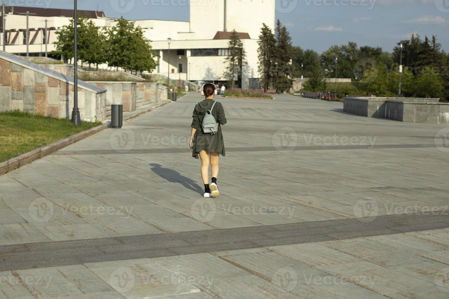Girl walks through square in summer. Walk around city. Girl with small backpack. photo