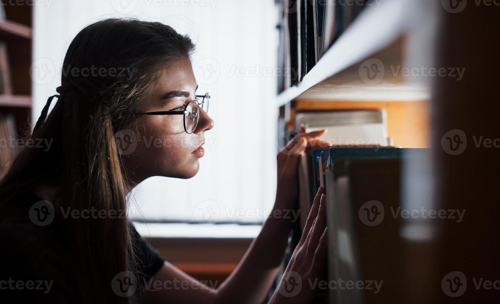 Searching for right information. Against window. Female student is in library that full of books. Conception of education photo