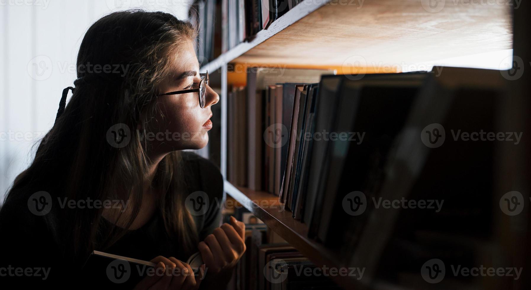 Searching for right information. Against window. Female student is in library that full of books. Conception of education photo