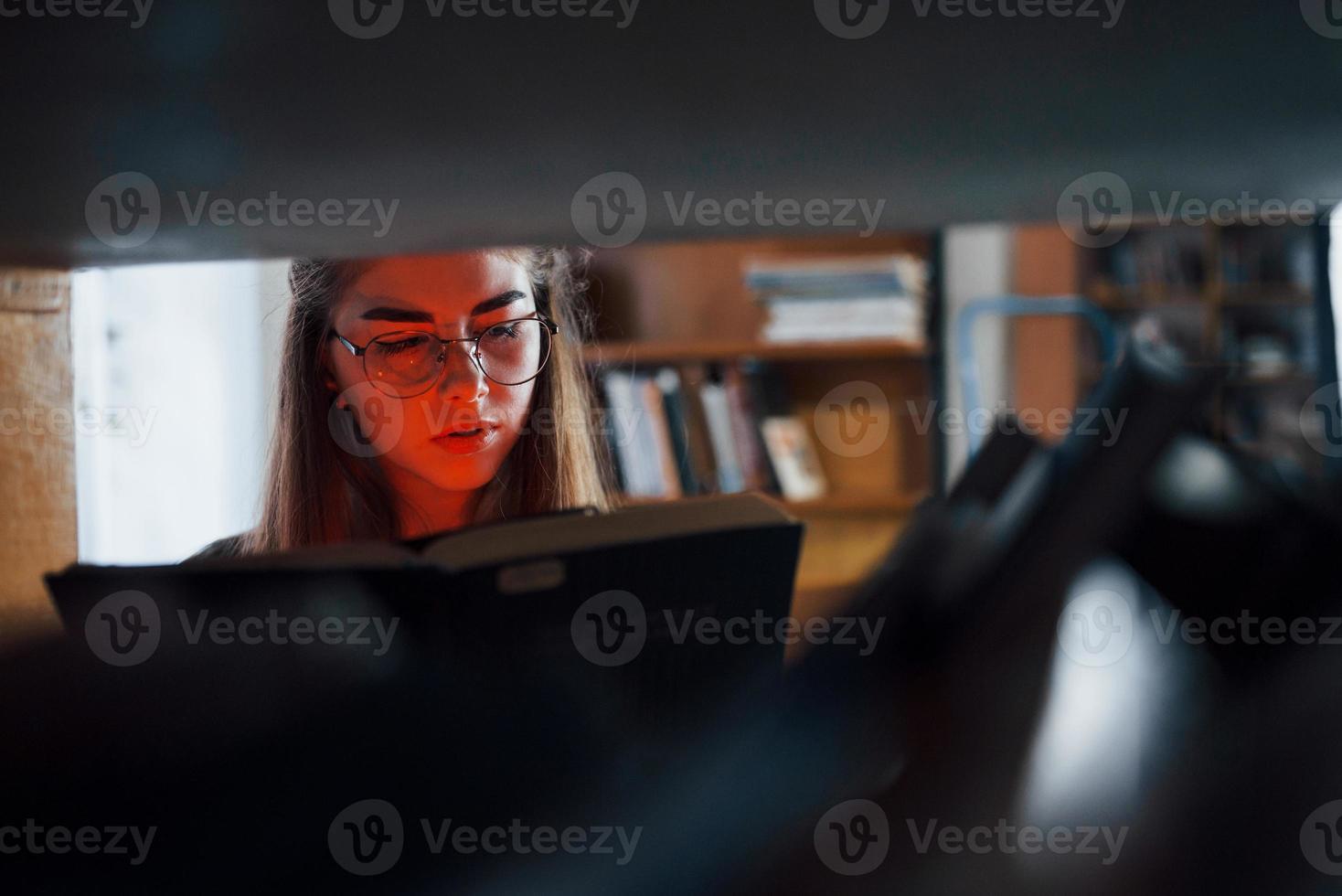 Artificial red light on from the book. Female student is in library that full of books. Conception of education photo