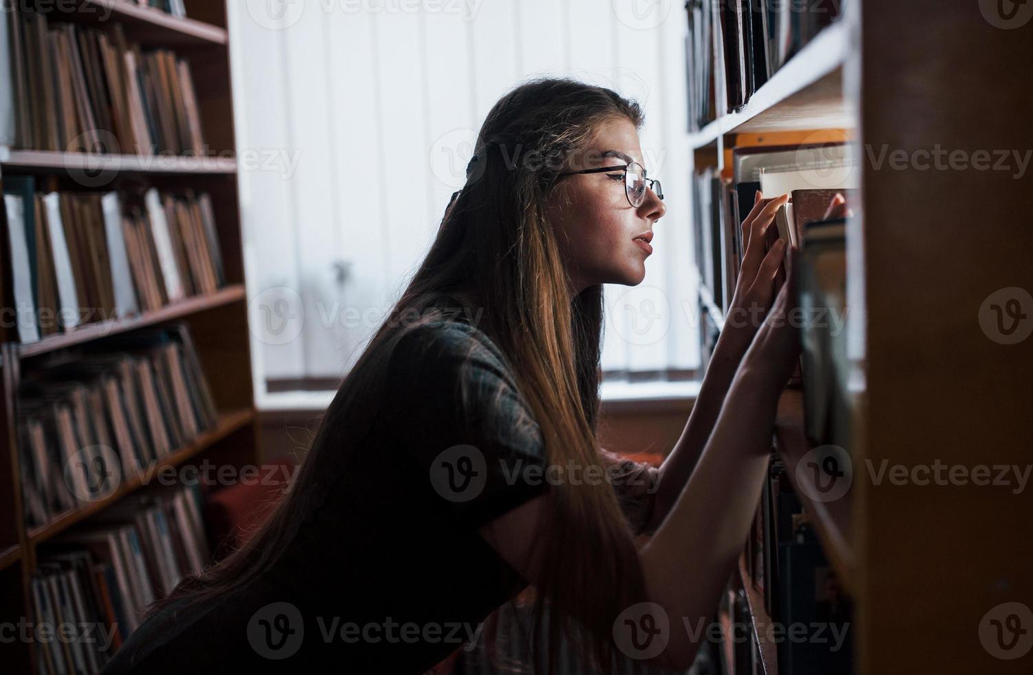 Searching for right information. Against window. Female student is in library that full of books. Conception of education photo