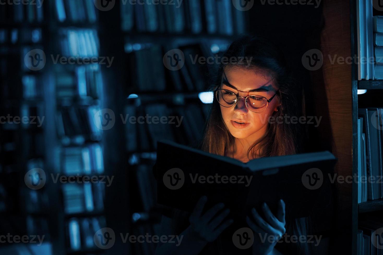 Light from the book in dark room. Imagination conception. Female student is in library that full of books. Conception of education photo