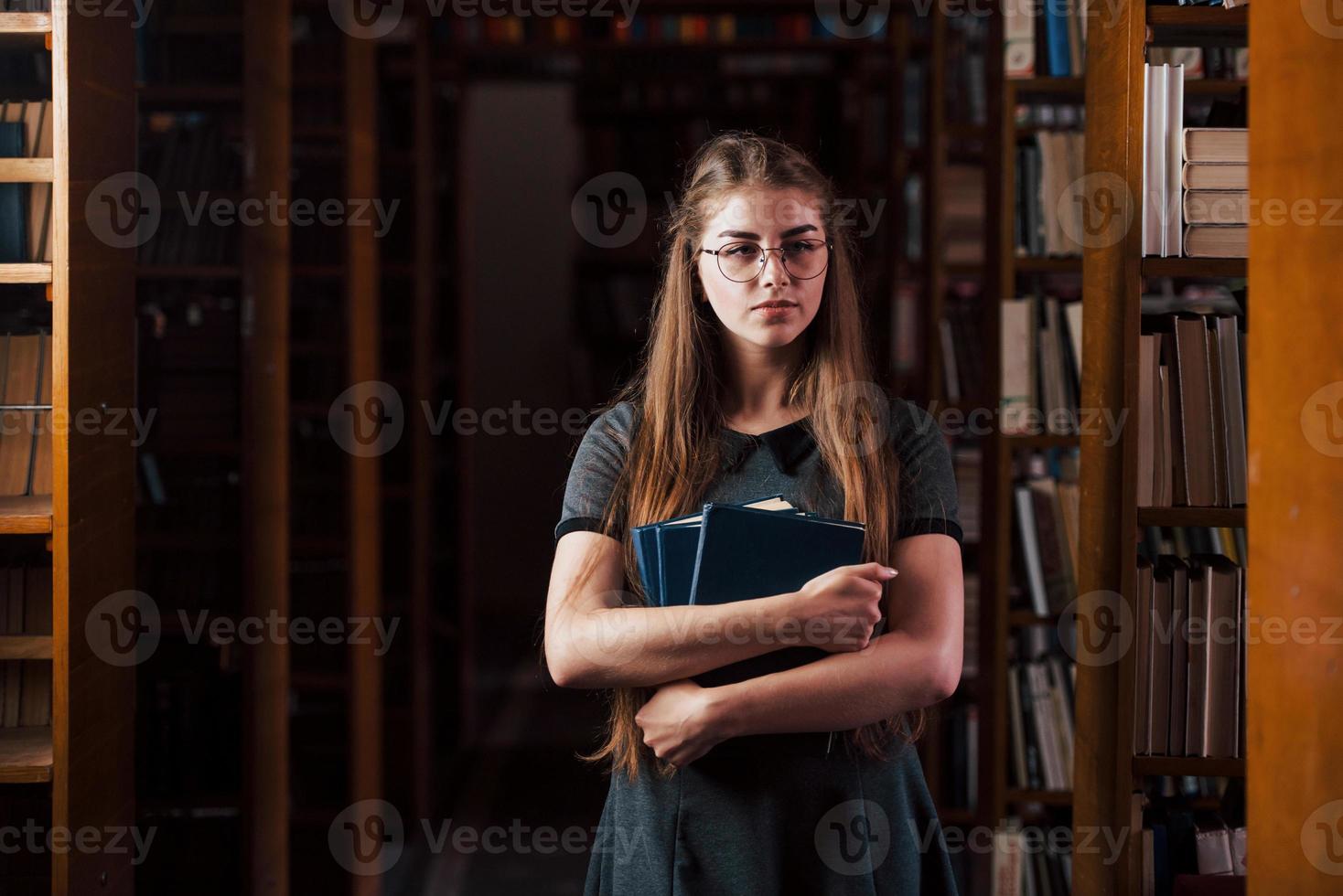 mira hacia la cámara. una estudiante está en una biblioteca llena de libros. concepción de la educación foto