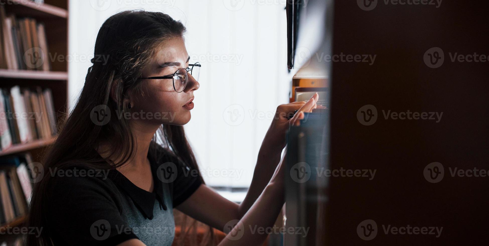 Searching for right information. Against window. Female student is in library that full of books. Conception of education photo