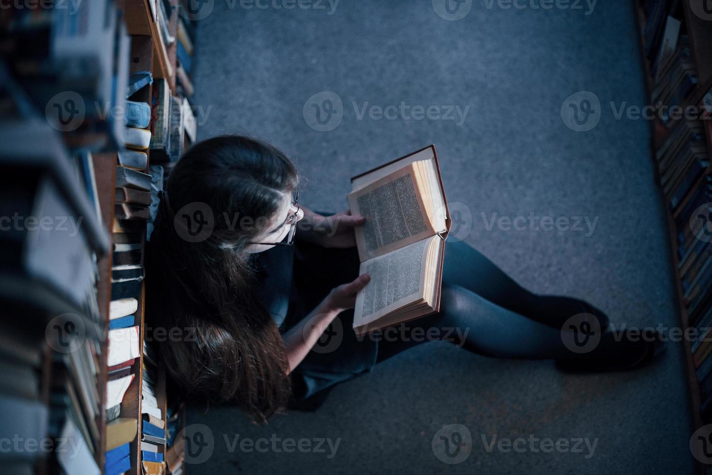 Top view. In skirt. Female student is in library that full of books. Conception of education photo