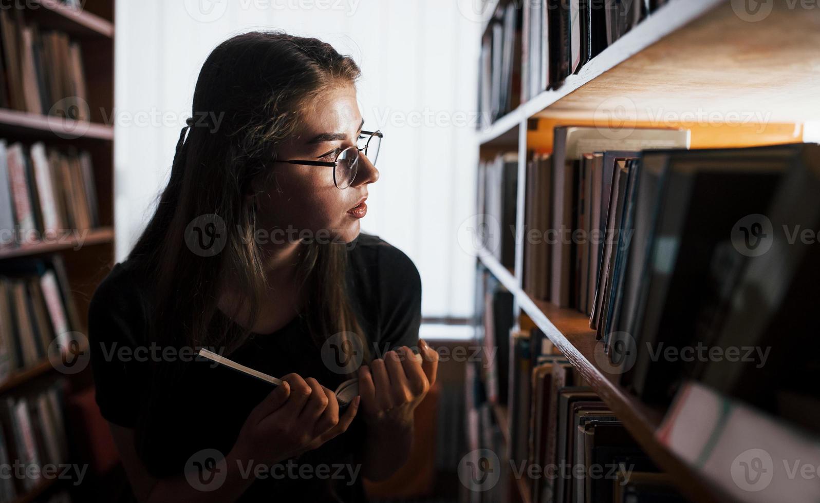 Searching for right information. Against window. Female student is in library that full of books. Conception of education photo