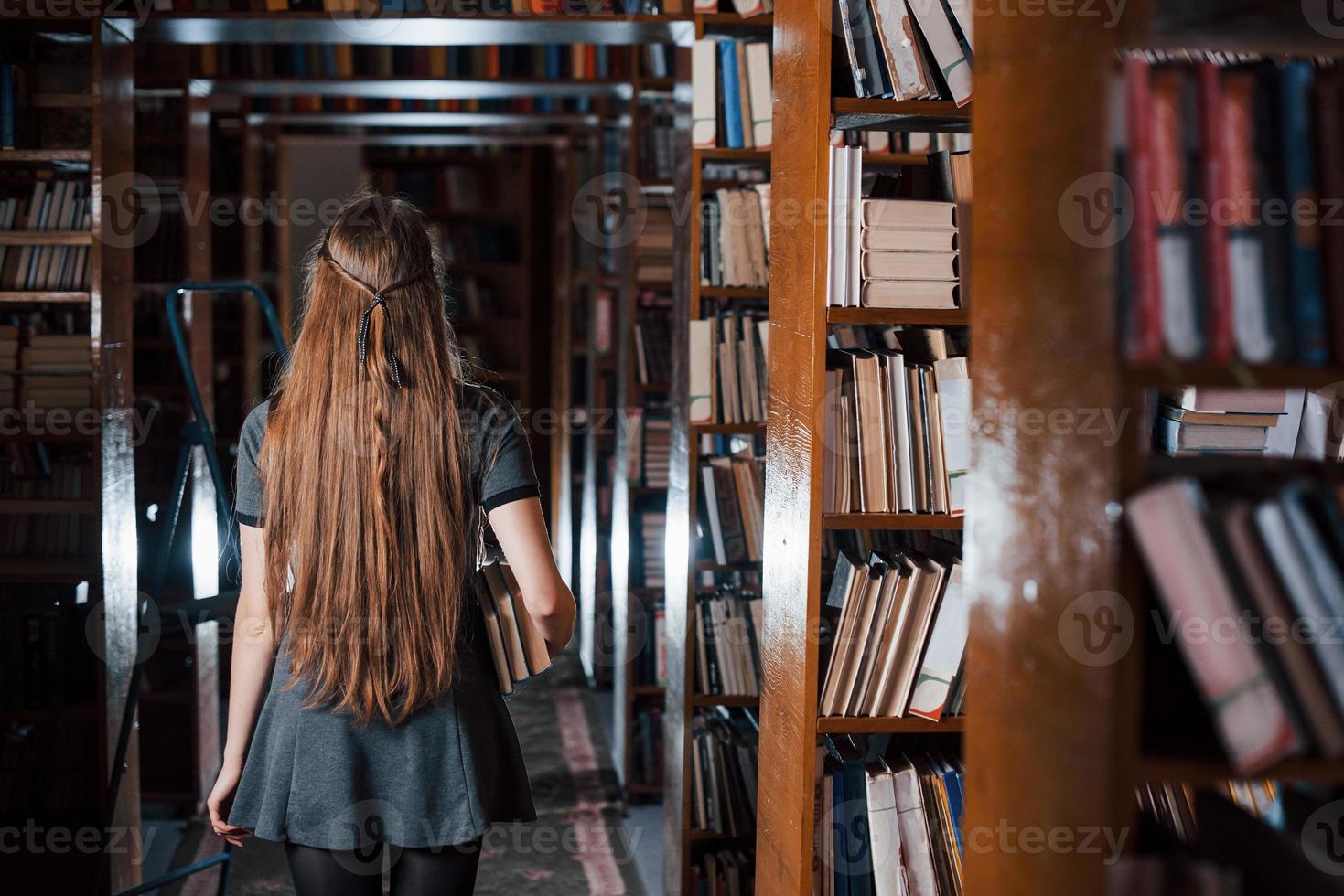 Back view. Female student is in library that full of books. Conception of education photo