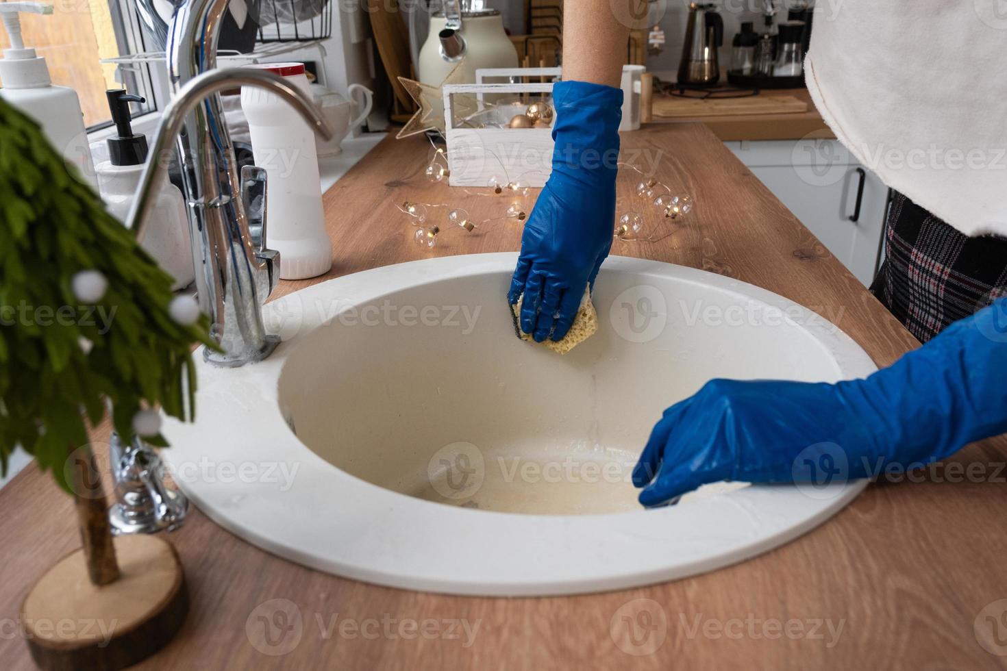 Cleaning sink in kitchen before the Christmas and New Year holidays. Hand in gloves and sponge, detergent, dry powder. Festive decor in the white kitchen, cozy interior of the home photo