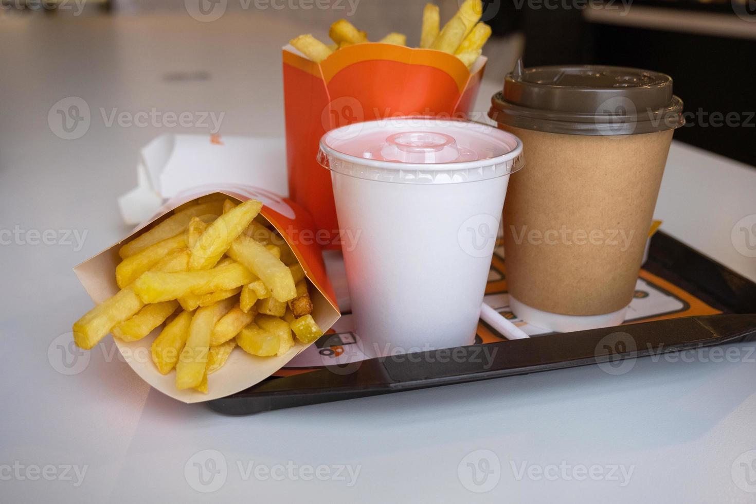 comida rápida en una bandeja en un restaurante. papas fritas, un vaso con batido, café foto