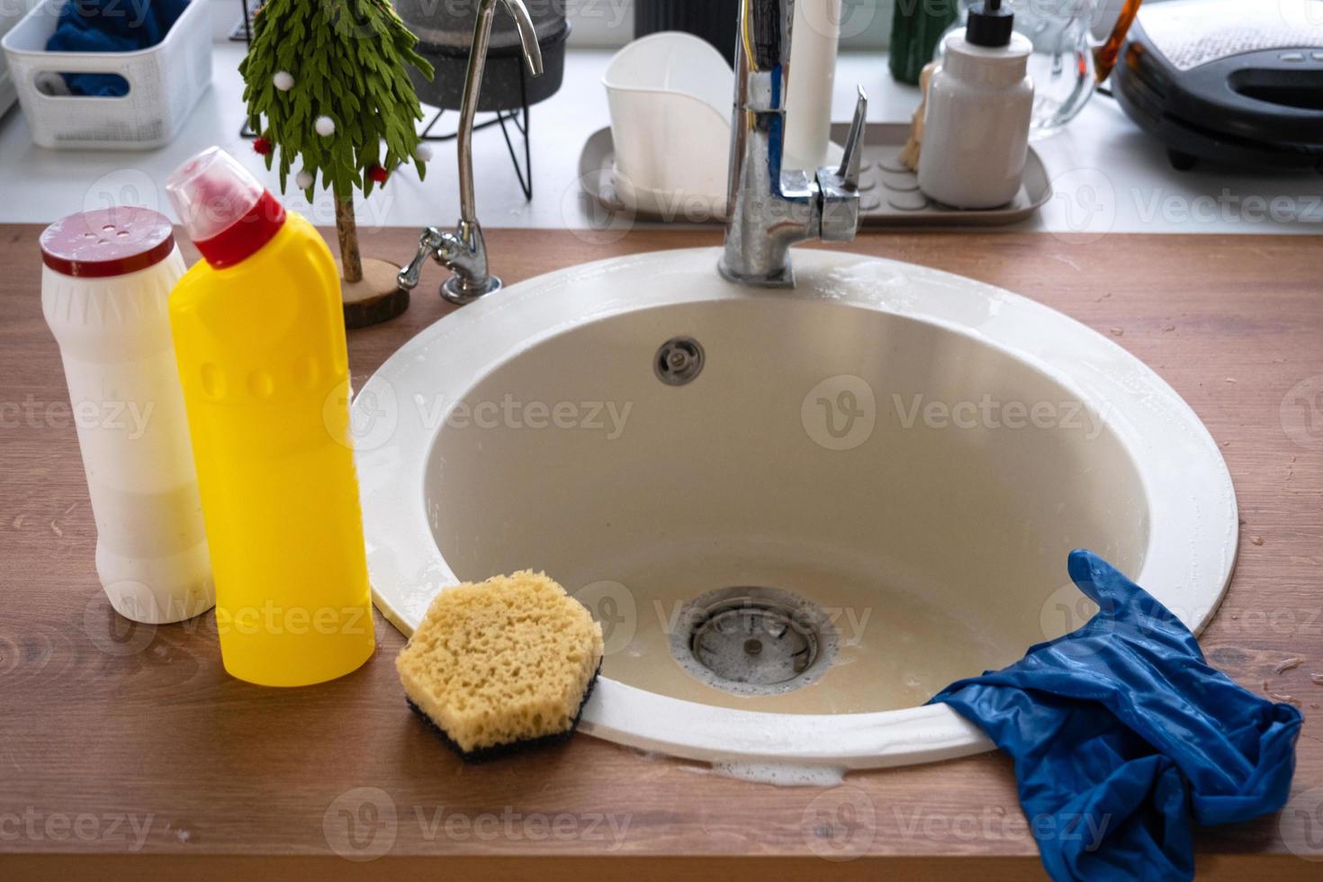 limpiar la cocina antes de las vacaciones de navidad y año nuevo. detergente, polvo seco, esponja, guantes en el fregadero. decoración festiva en la cocina blanca, acogedor interior de la casa foto