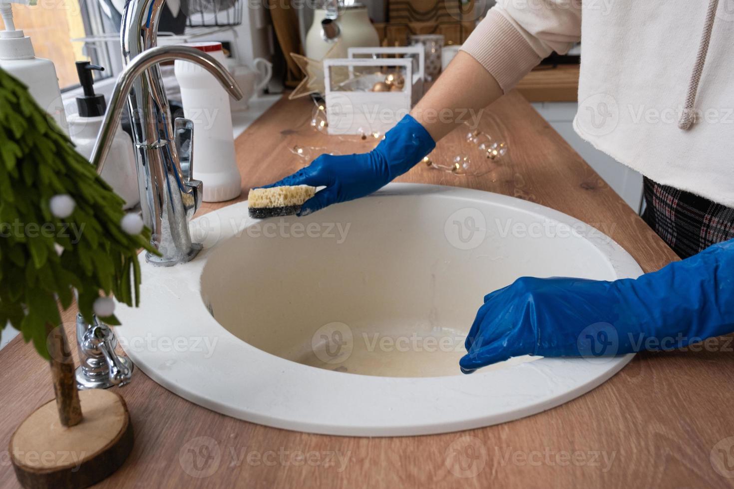 Cleaning sink in kitchen before the Christmas and New Year holidays. Hand in gloves and sponge, detergent, dry powder. Festive decor in the white kitchen, cozy interior of the home photo