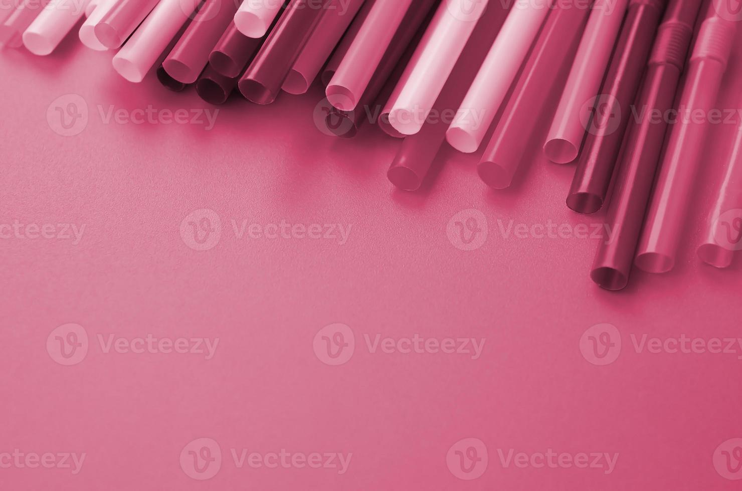 Many colorful straws for drinks lies on a bright orange background surface Image toned in Viva Magenta, color of the year photo