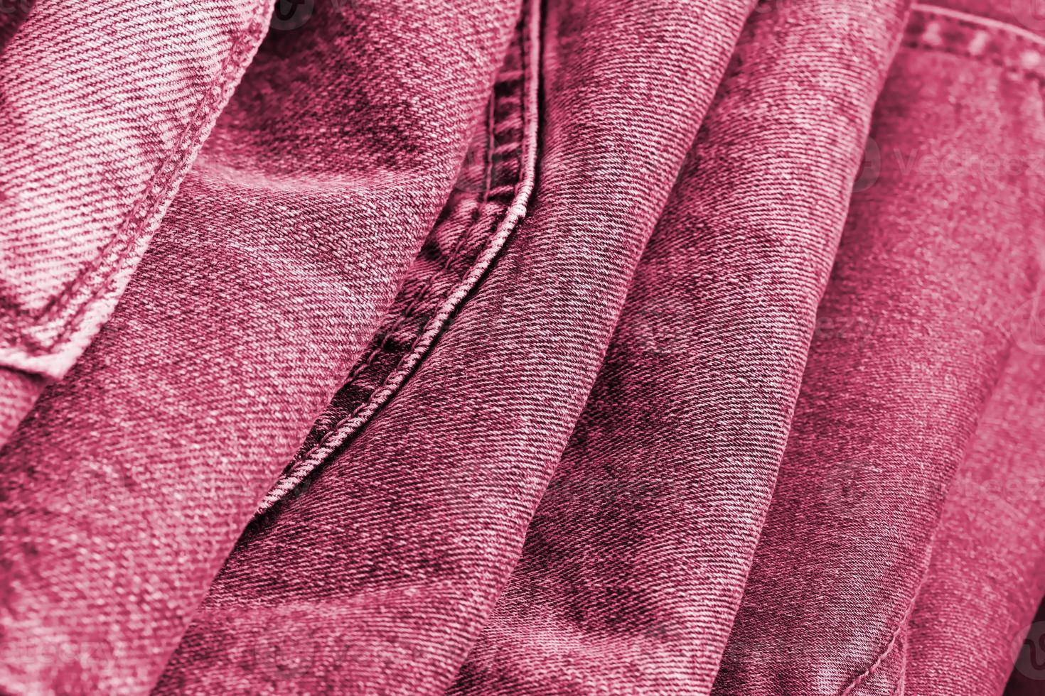 Many jeans in stack in wardrobe room. Row of pants denim jeans in closet. Concept of buy, sell, shopping and fashionable clothes Image toned in Viva Magenta, color of the 2023 year photo