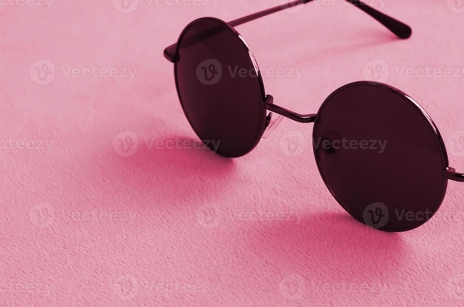 elegantes gafas de sol negras con gafas redondas se encuentran sobre una manta hecha de tela de lana suave y esponjosa. imagen tonificada en viva magenta, color del año 2023 foto