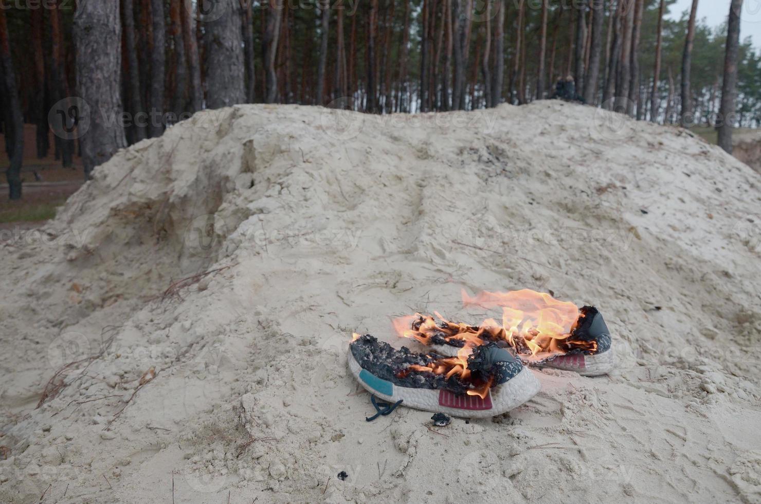 Burning sports sneakers or gym shoes on fire stand on sandy beach coast. Athlete burned out. Physical exertion during training concept photo