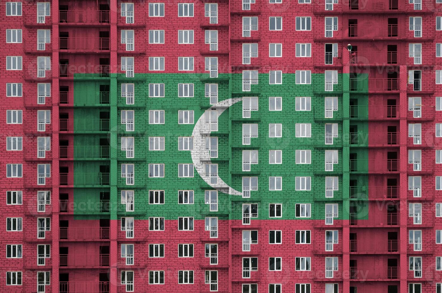 Maldives flag depicted in paint colors on multi-storey residental building under construction. Textured banner on brick wall background photo