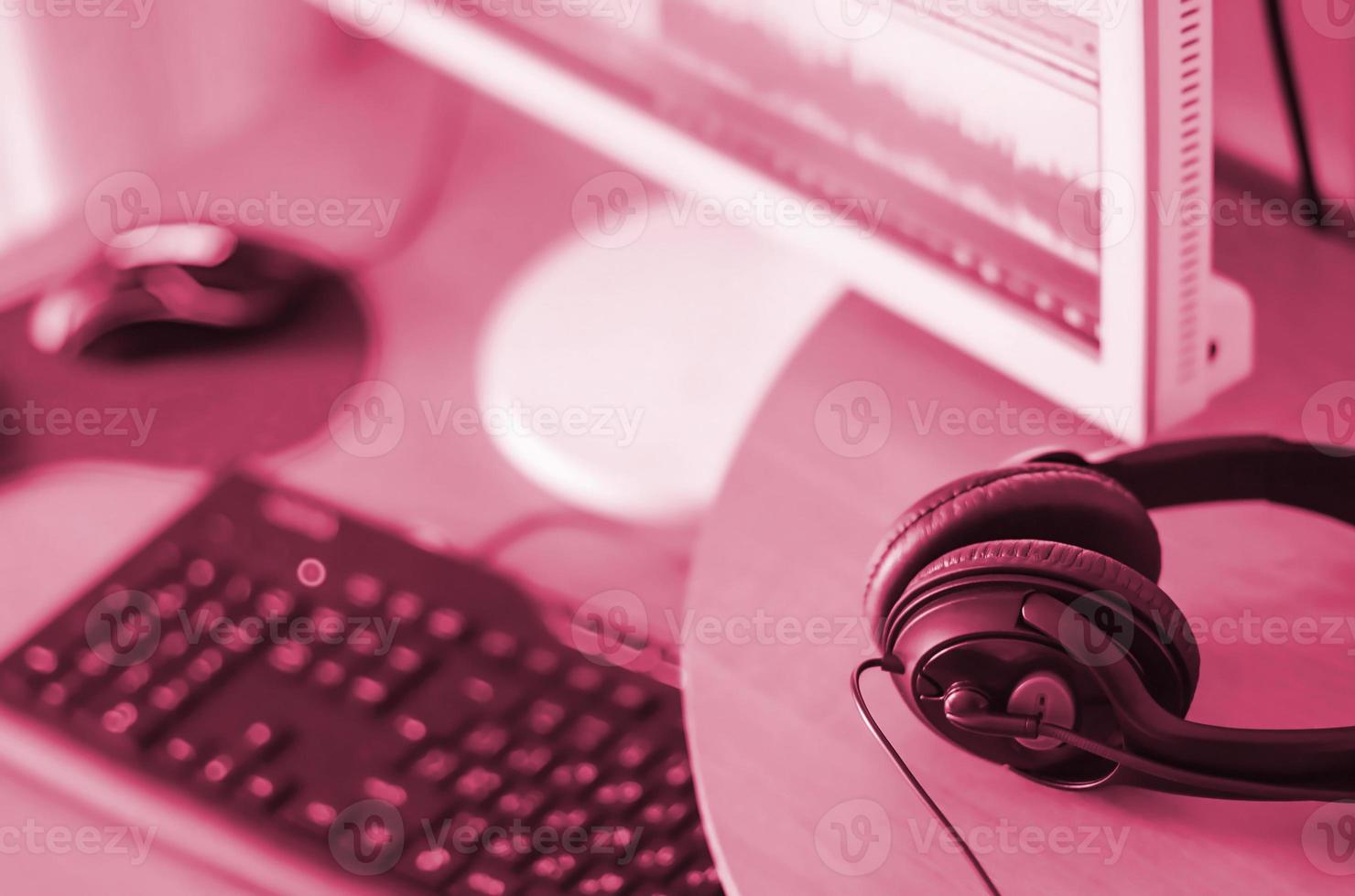 Big black headphones lie on the wooden desktop of the sound designer. Image toned in Viva Magenta, color of the 2023 year photo