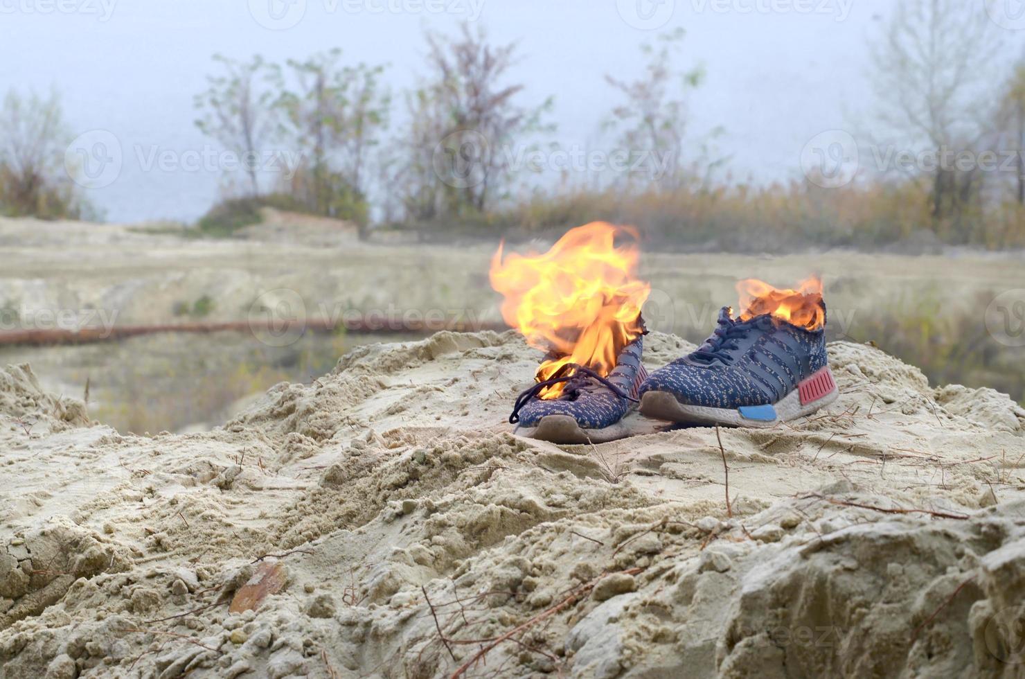 Burning sports sneakers or gym shoes on fire stand on sandy beach coast
