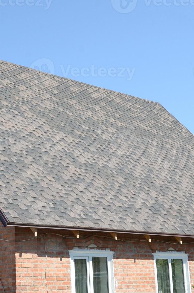 Flexible shingles of bitumen roofing surface on the brick house photo
