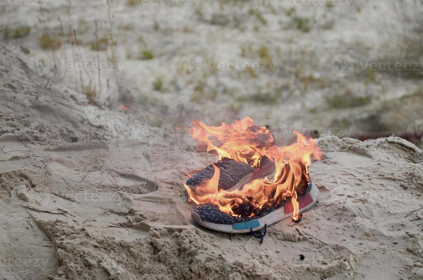 Burning sports sneakers or gym shoes on fire stand on sandy beach coast. Athlete burned out. Physical exertion during training concept photo