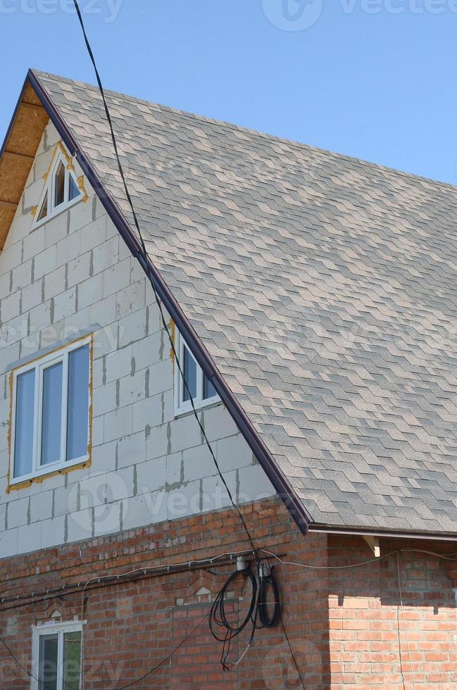 Flexible shingles of bitumen roofing surface on the brick house photo