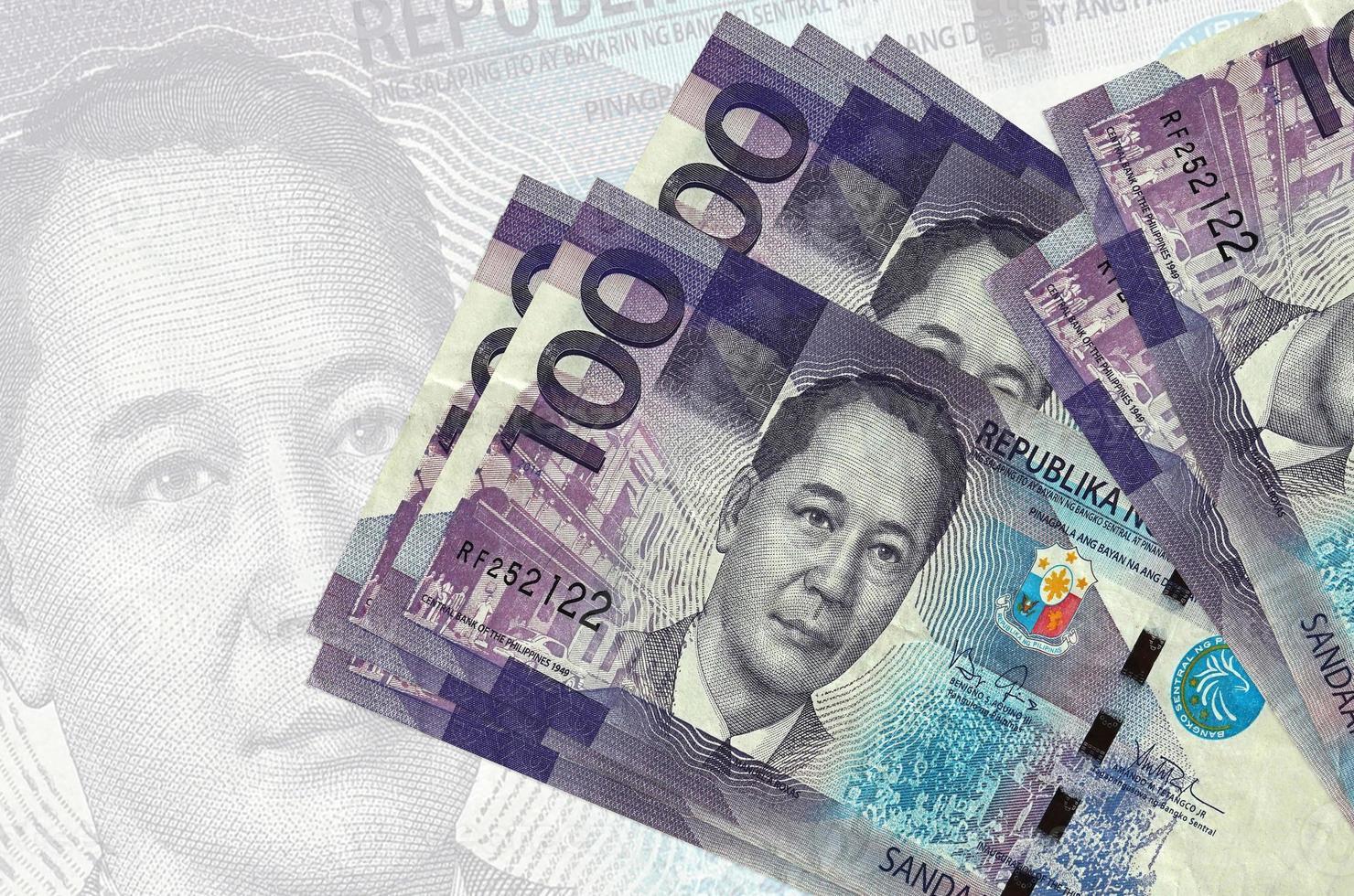 100 billetes de piso filipino se encuentran apilados sobre el fondo de un gran billete semitransparente. presentación abstracta de la moneda nacional foto