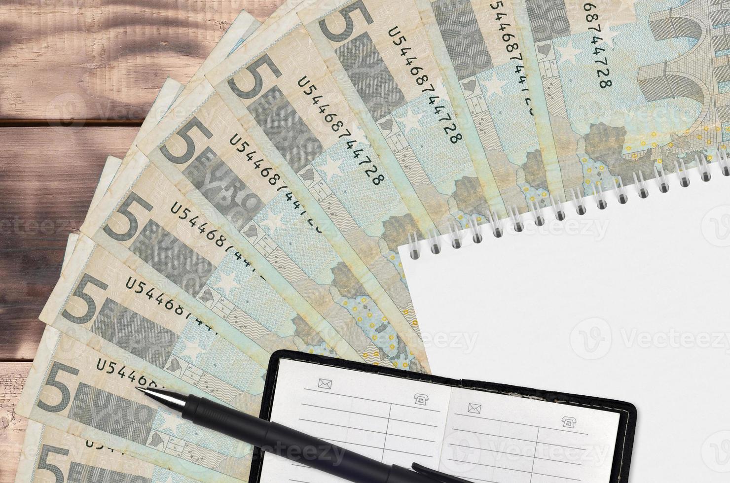 Abanico de billetes de 5 euros y bloc de notas con libreta de contactos y bolígrafo negro. concepto de planificación financiera y estrategia empresarial foto