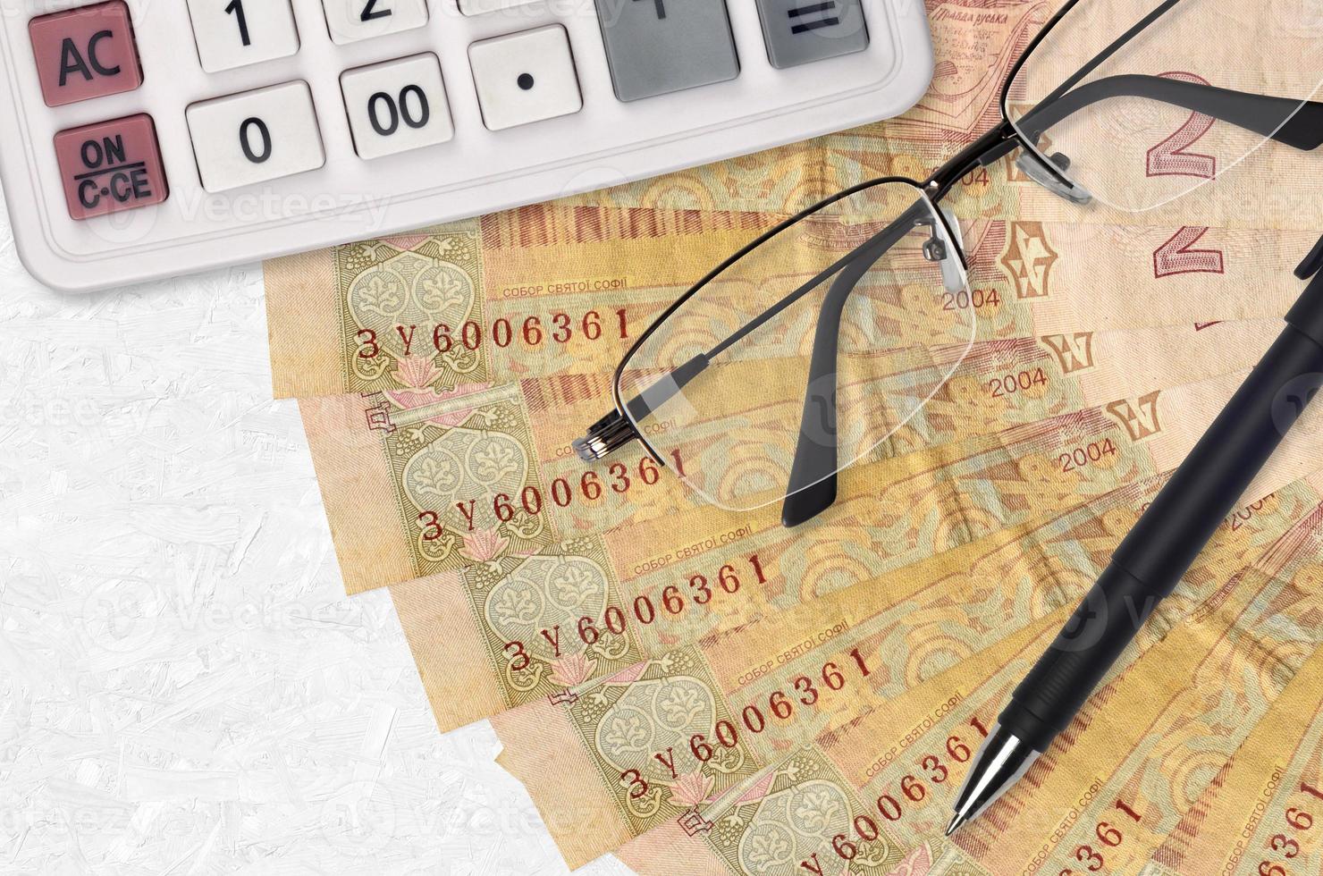 2 Ukrainian hryvnias bills fan and calculator with glasses and pen. Business loan or tax payment season concept photo