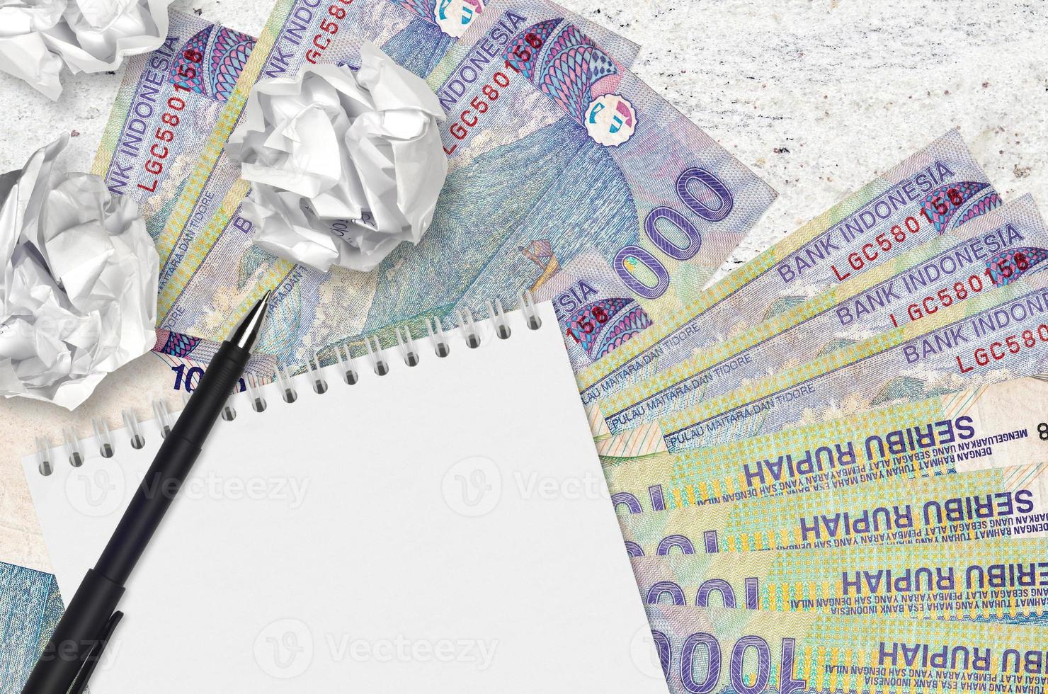 1000 Indonesian rupiah bills and balls of crumpled paper with blank notepad. Bad ideas or less of inspiration concept. Searching ideas for investment photo