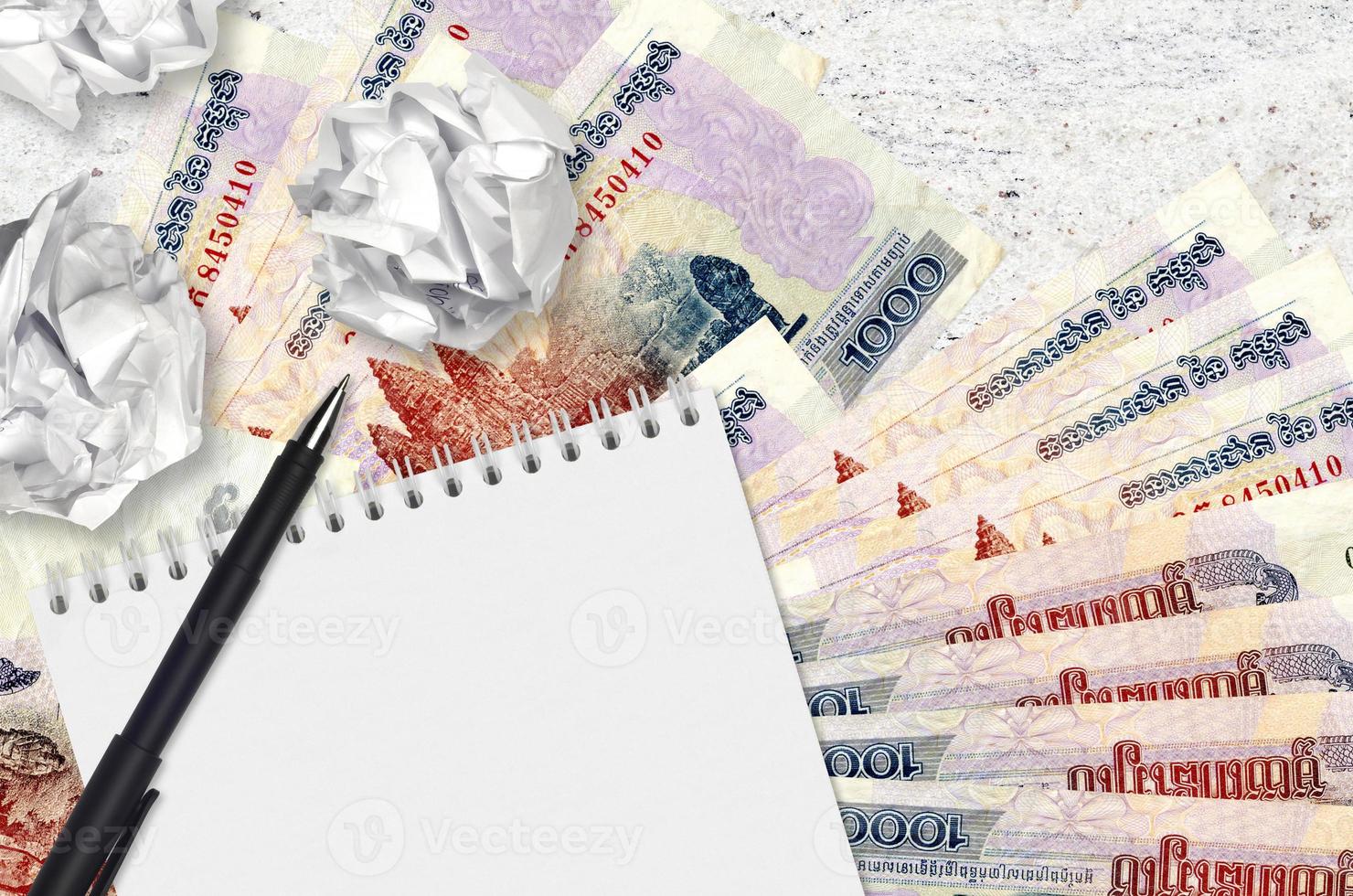 1000 Cambodian riels bills and balls of crumpled paper with blank notepad. Bad ideas or less of inspiration concept. Searching ideas for investment photo