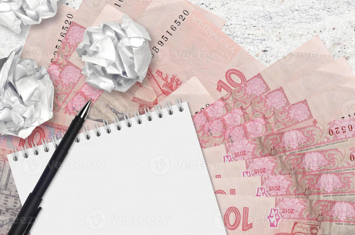 10 Ukrainian hryvnias bills and balls of crumpled paper with blank notepad. Bad ideas or less of inspiration concept. Searching ideas for investment photo