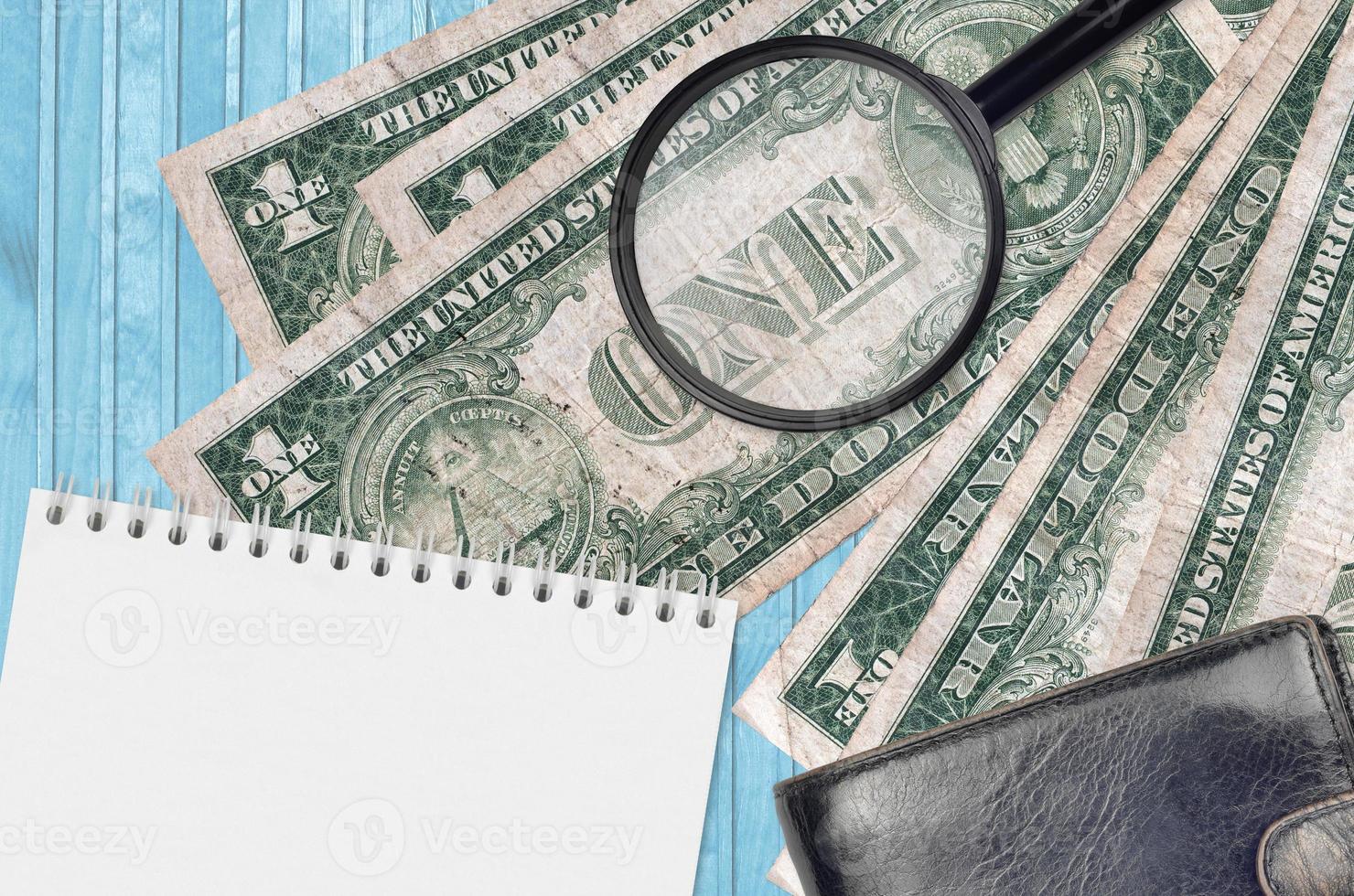 1 US dollar bills and magnifying glass with black purse and notepad. Concept of counterfeit money. Search for differences in details on money bills to detect fake photo