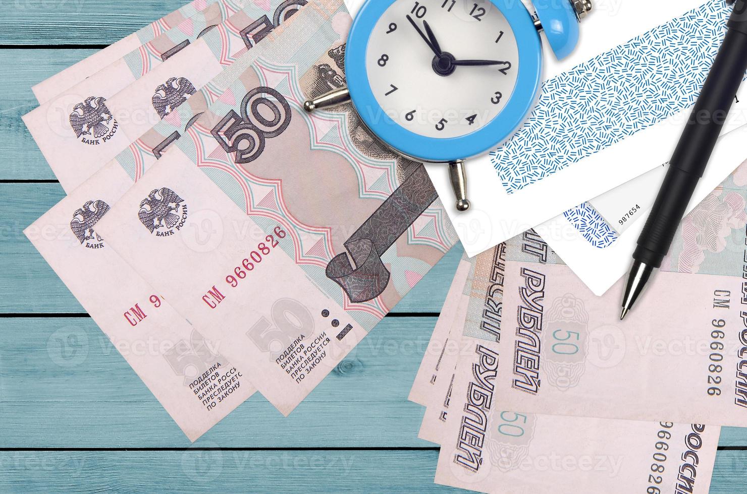 50 russian rubles bills and alarm clock with pen and envelopes. Tax season concept, payment deadline for credit or loan. Financial operations using postal service photo