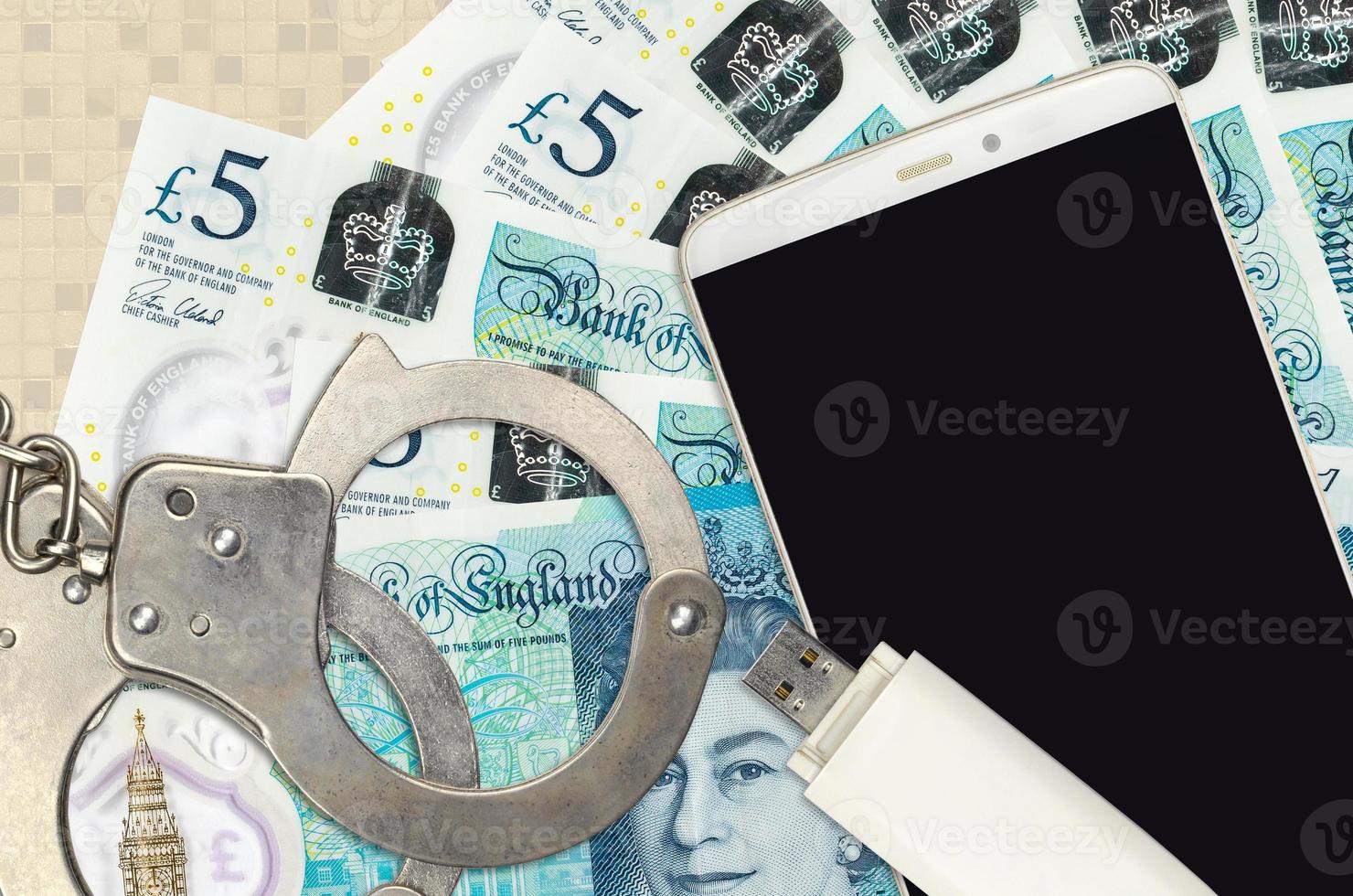 5 British pounds bills and smartphone with police handcuffs. Concept of hackers phishing attacks, illegal scam or malware soft distribution photo