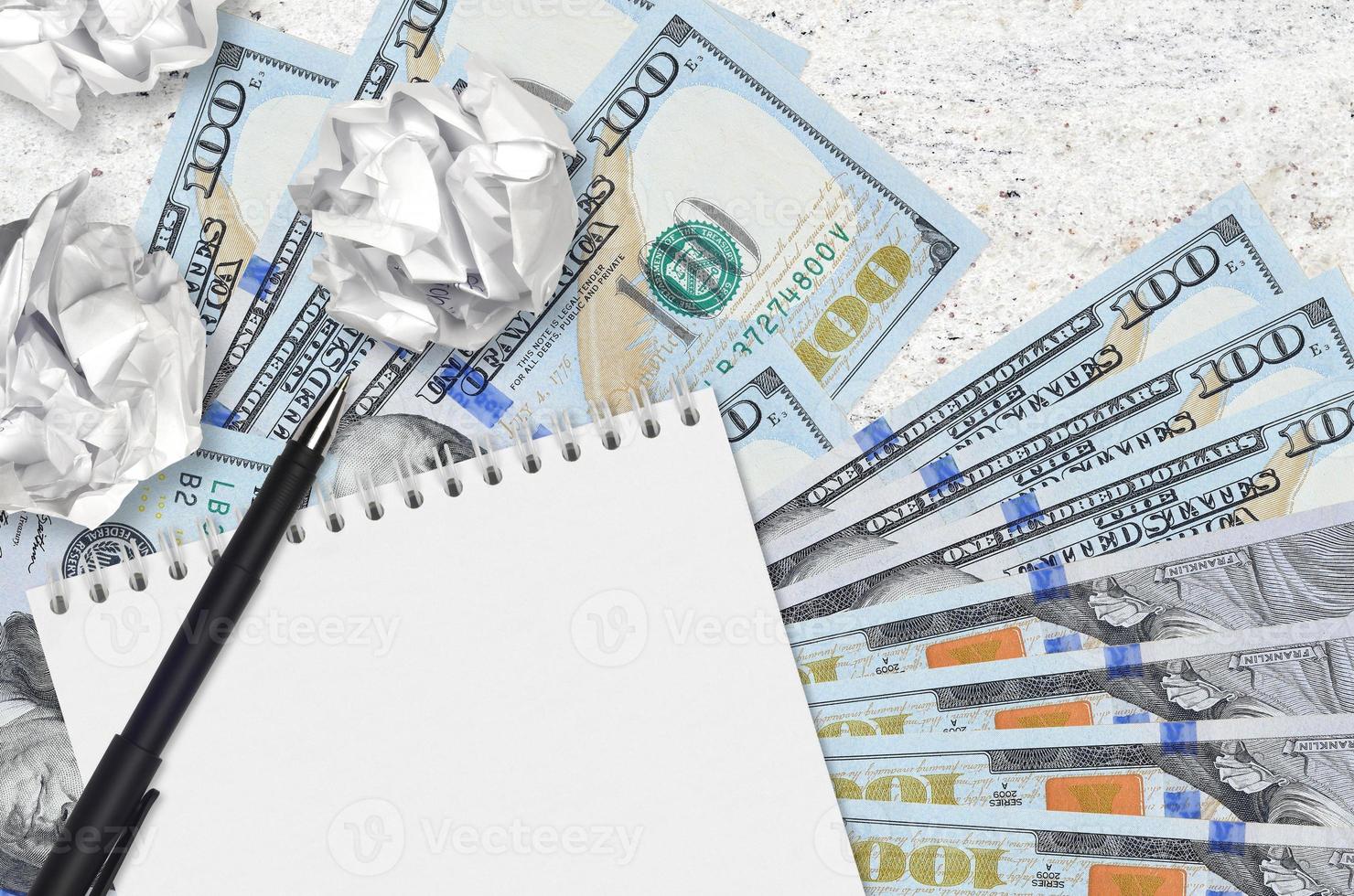 Billetes de 100 dólares estadounidenses y bolas de papel arrugado con bloc de notas en blanco. malas ideas o menos concepto de inspiración. buscando ideas de inversión foto