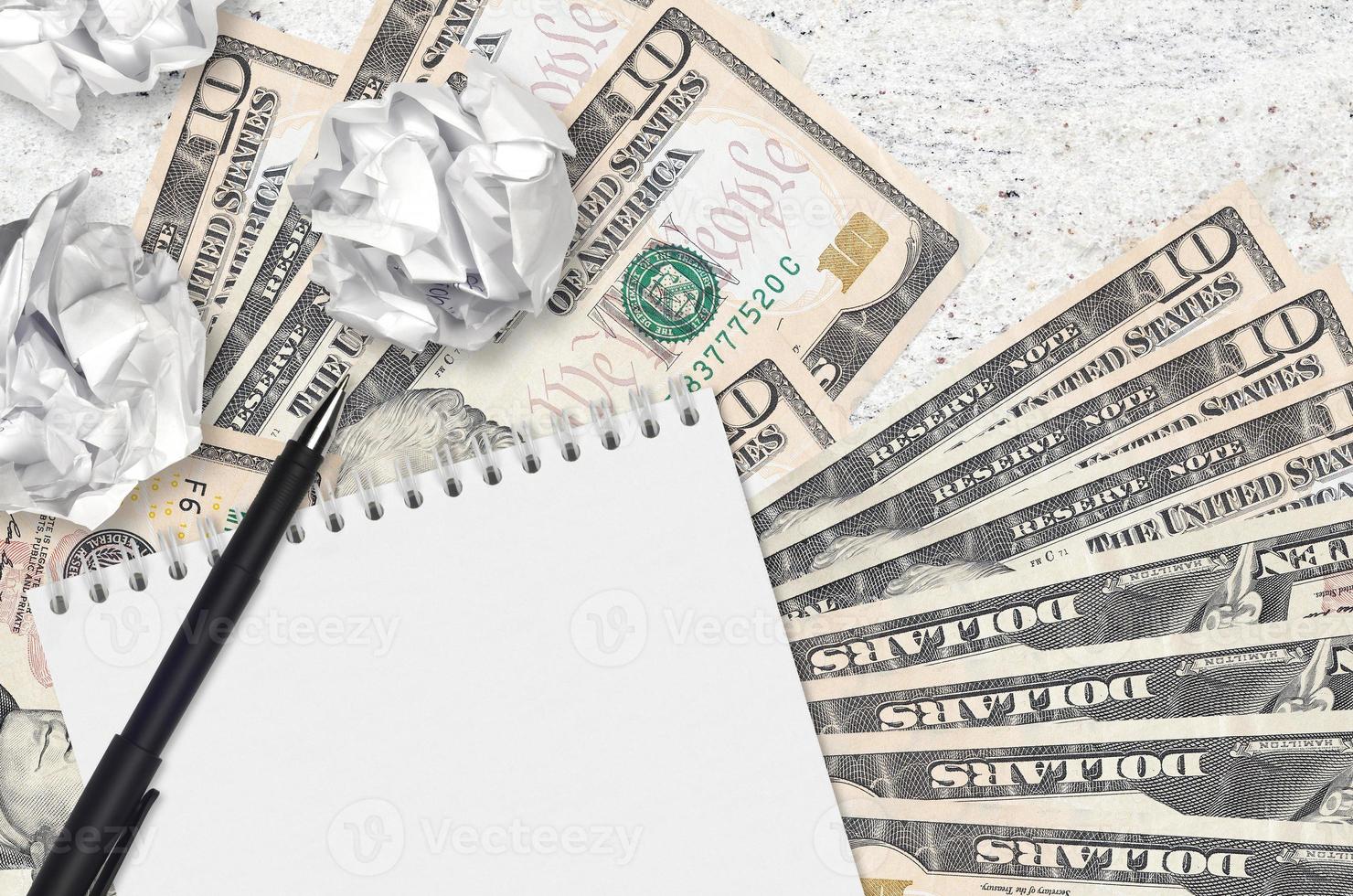 10 US dollars bills and balls of crumpled paper with blank notepad. Bad ideas or less of inspiration concept. Searching ideas for investment photo