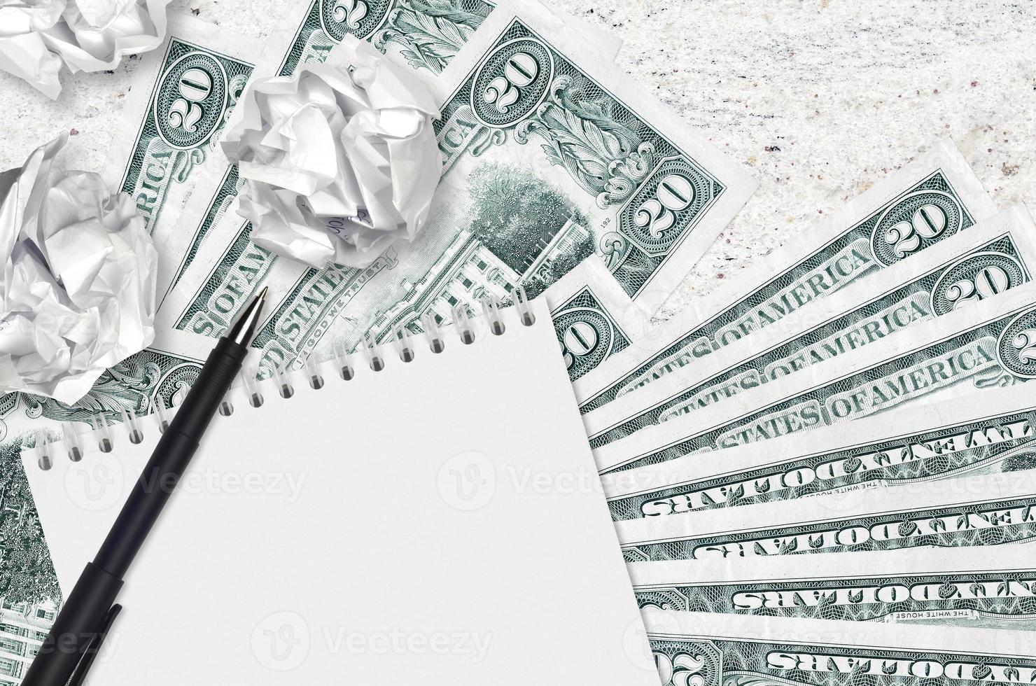 20 US dollars bills and balls of crumpled paper with blank notepad. Bad ideas or less of inspiration concept. Searching ideas for investment photo