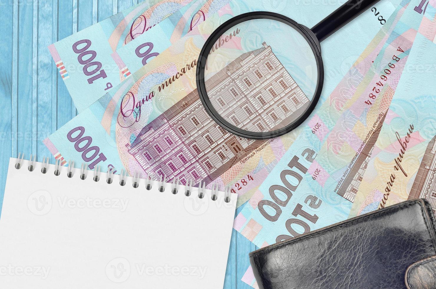 1000 Ukrainian hryvnias bills and magnifying glass with black purse and notepad. Concept of counterfeit money. Search for differences in details on money bills to detect fake photo